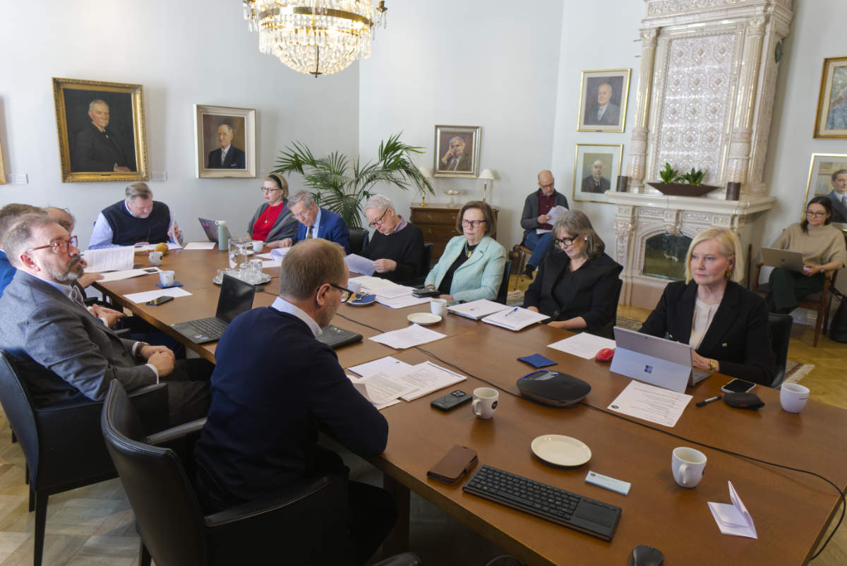 Ett femtontal personer samlade till SFV:s ordinarie föreningsmöte på SFV:s kansli, runt det avlånga styrelsebordet. Rummet är kantat av porträtt, från taket hänger en stor kristallkrona.