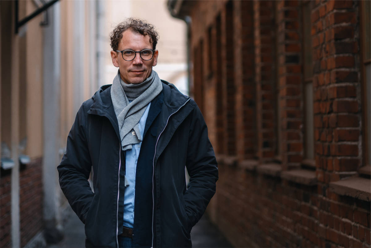 Juha Itkonen står i smal gränd. Det fins en röd tegelvägg till höger